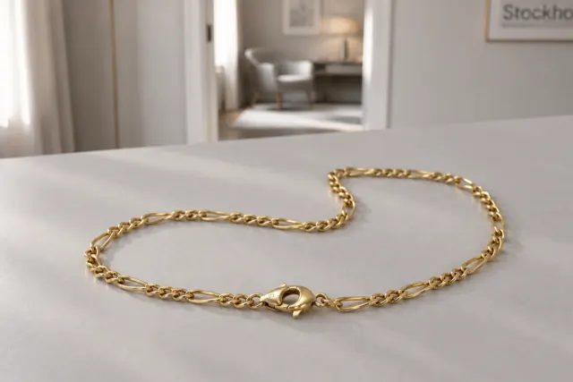 Figarolänk halsband i guld som ligger på ett ljust bord